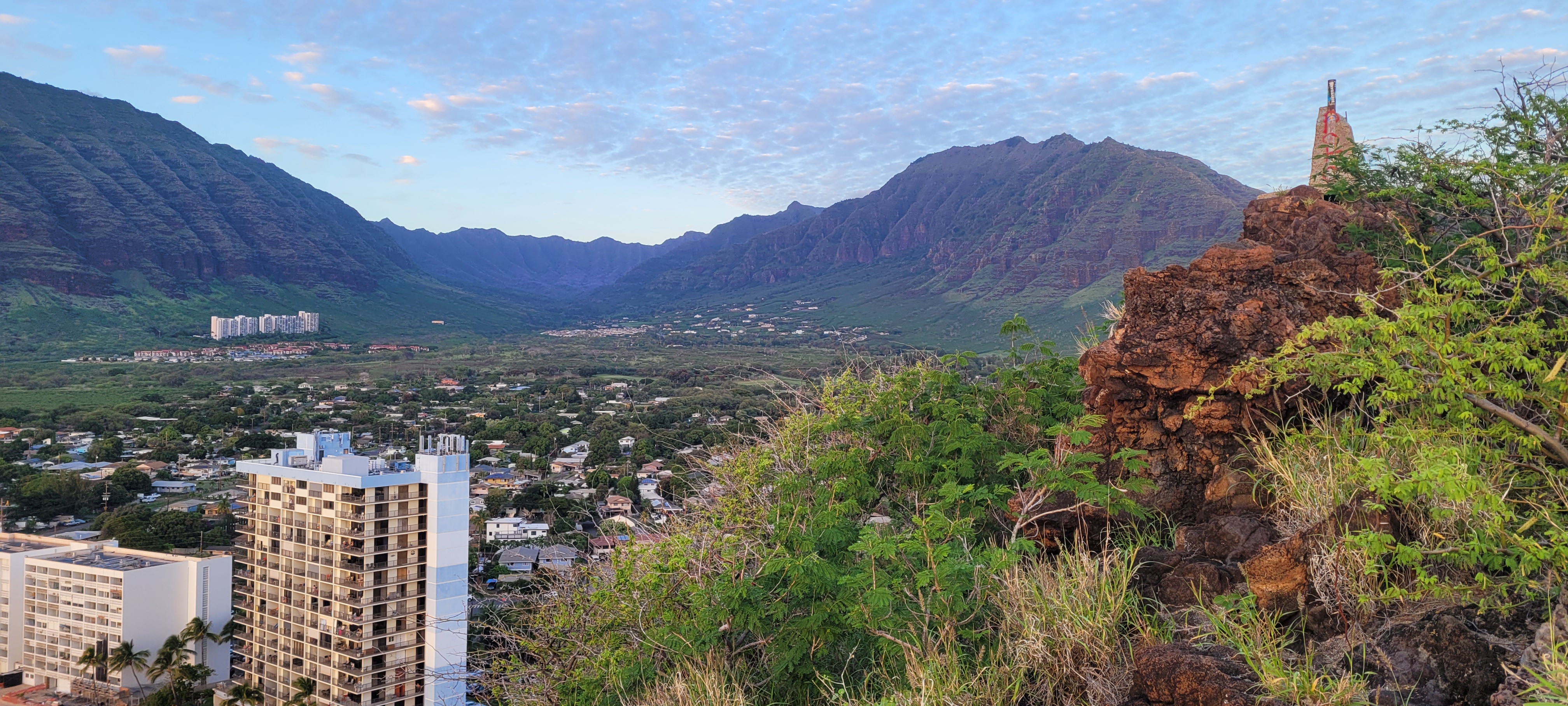 A green valley of volcanic rock, steep cliffsides, with a neighborhood in the foreground.