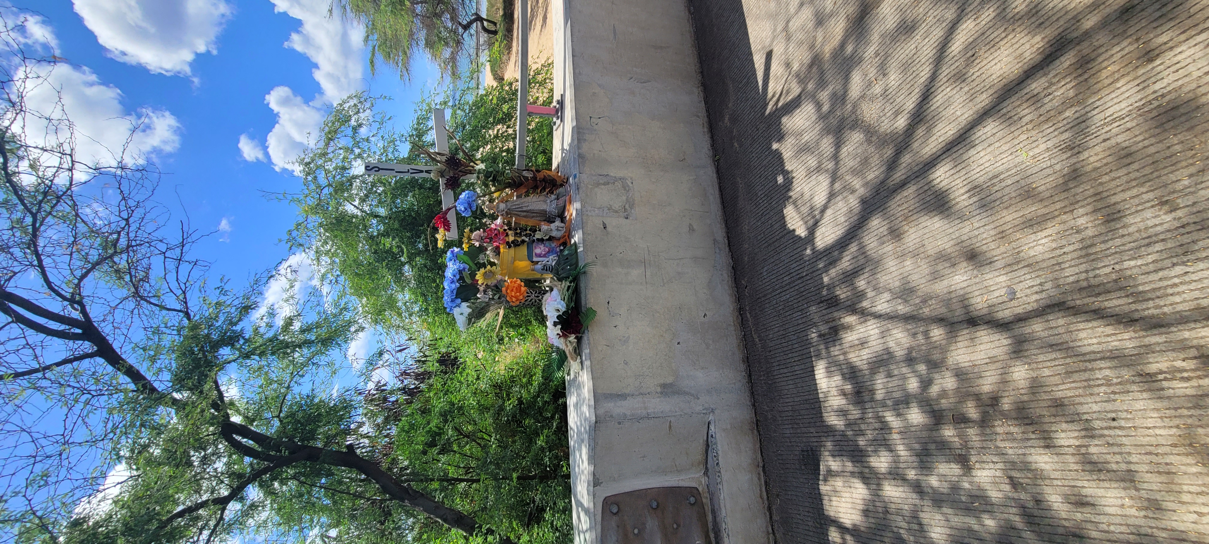 A bundle of lei, vase, offerings, a cross and a photo, at the end of a bridge.