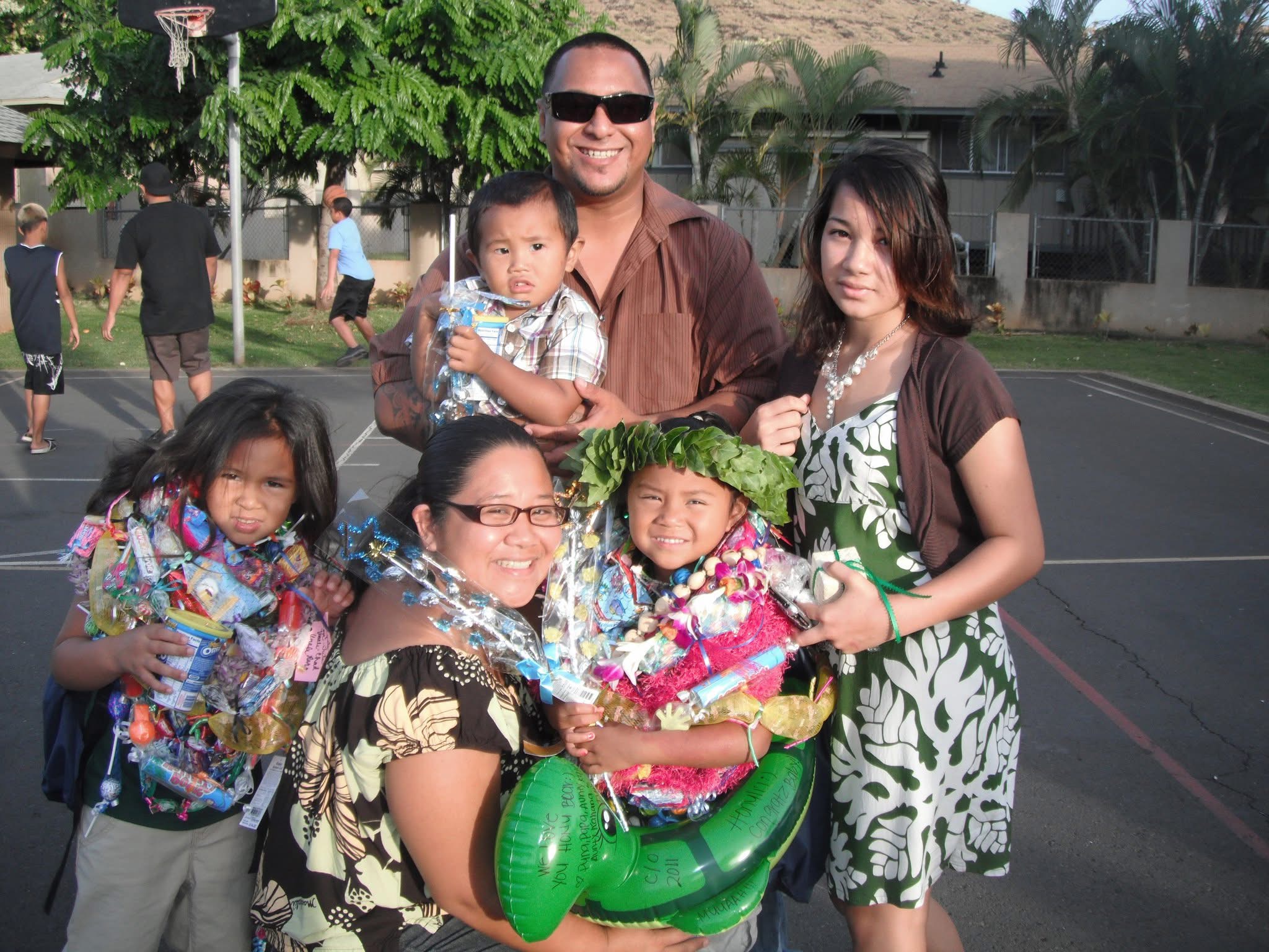 A hawaiian man standing with his family, on a playground